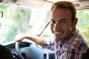 Portrait of young man looking at camera while sitting on cars fr