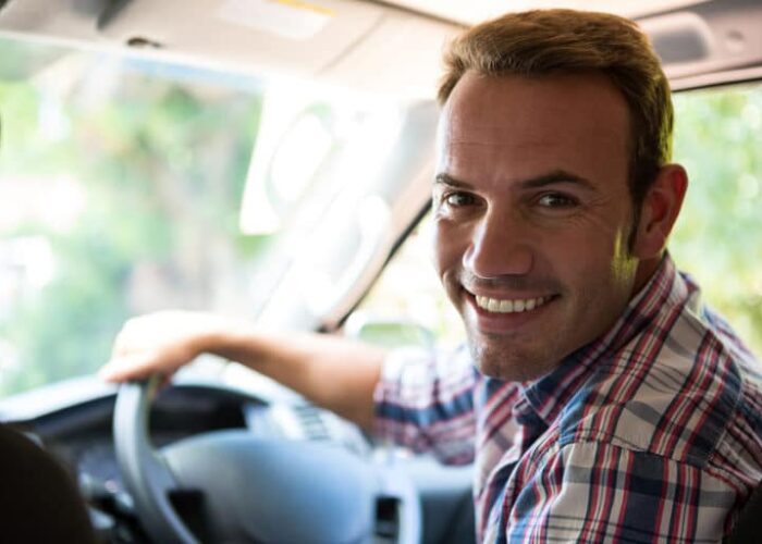 Portrait of young man looking at camera while sitting on cars fr